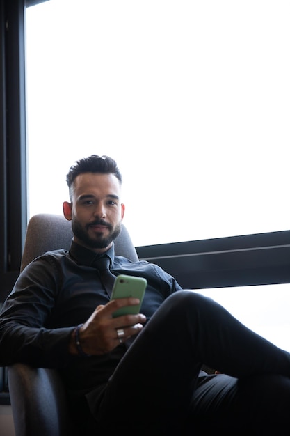 Photo beau jeune homme portant une barbe assis regardant son téléphone, homme répondant à un message sur un téléphone portable