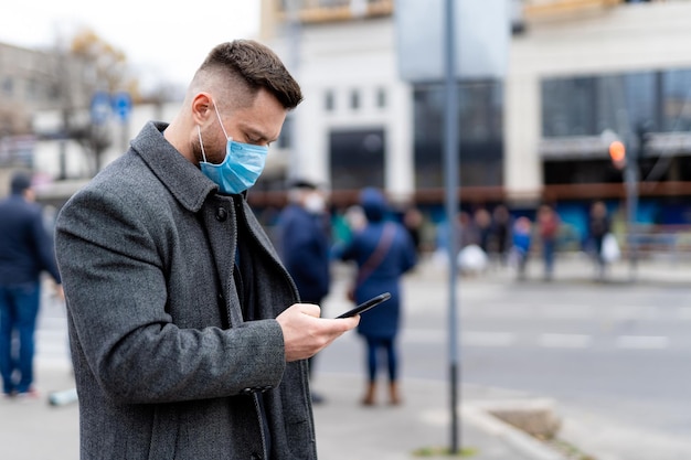 Beau jeune homme portant un masque de protection marchant dans la rue Homme d'affaires confiant regardant le smartphone tout en marchant à l'extérieur pendant l'automne photo stock