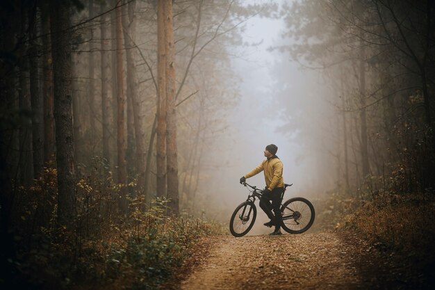 Beau jeune homme prenant un frein pendant le vélo à travers la forêt d'automne