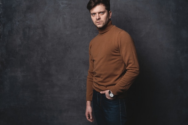 Beau jeune homme à la recherche. Portrait de jeune homme avec les mains dans les poches appuyé contre le mur gris.