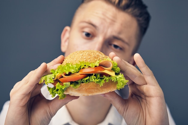 Beau jeune homme regardant un hamburger frais