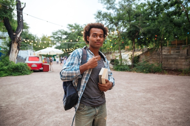 Beau jeune homme avec sac à dos et livres debout à l'extérieur