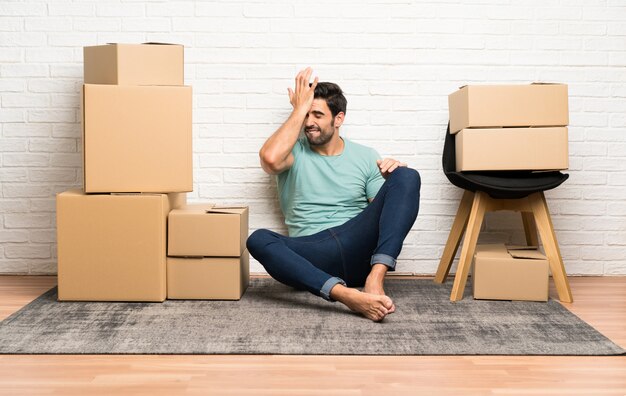 Beau jeune homme se déplaçant dans la nouvelle maison parmi les boîtes ayant des doutes avec l&#39;expression du visage confus