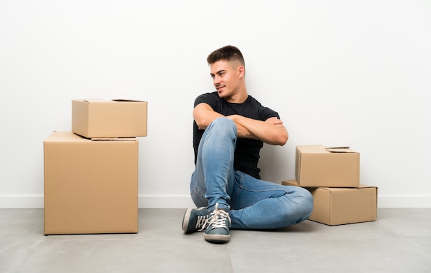 Beau jeune homme se déplaçant dans la nouvelle maison parmi les boîtes à la recherche sur le côté