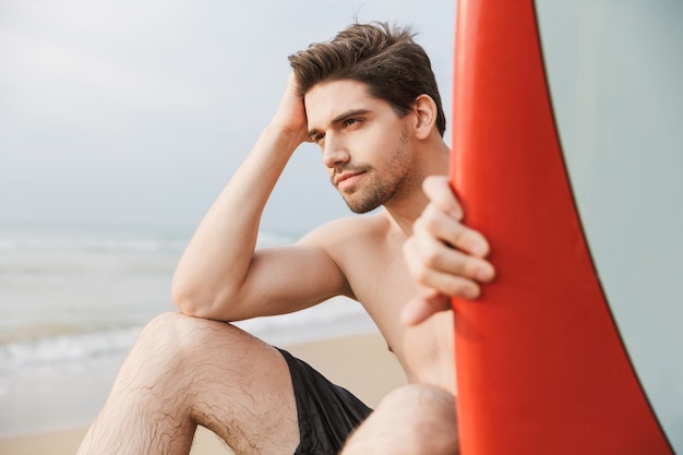 Beau jeune homme se détendre sur une plage avec planche de surf