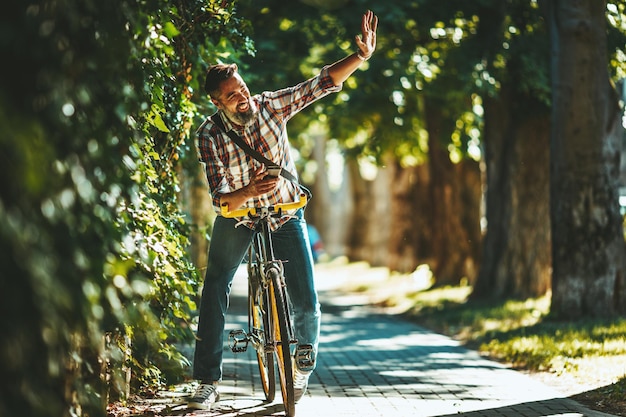 Un beau jeune homme se rend en ville avec son vélo, s'assied dessus et salue quelqu'un.