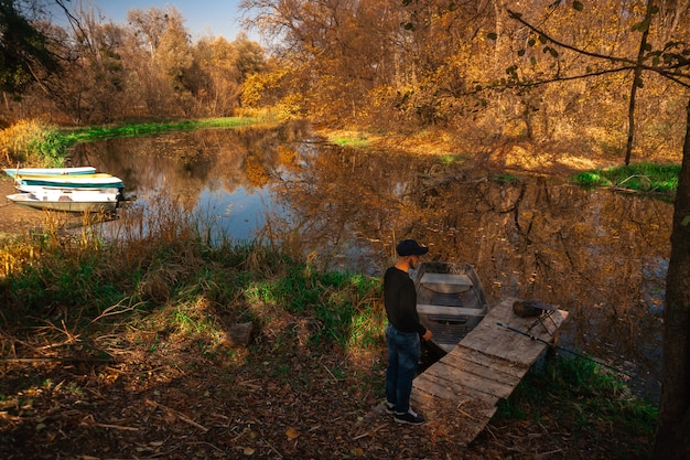 Beau jeune homme se tient au bord de la rivière en automne