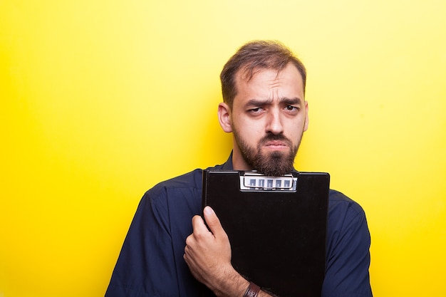 Beau jeune homme séduisant faisant des grimaces. Il tient un presse-papiers dans ses mains. Fond jaune