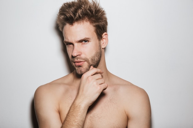 Beau jeune homme séduisant torse nu posant isolé sur mur blanc, regardant à l'avant