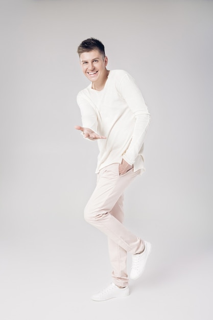 Beau jeune homme souriant dans un pull blanc étend sa main en avant isolé