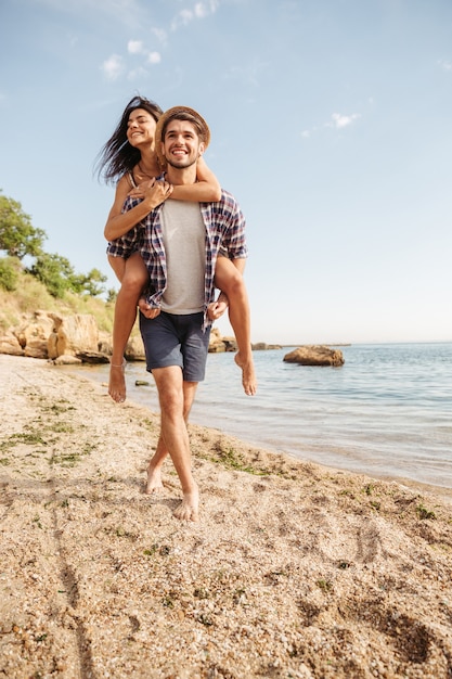 Beau jeune homme souriant donnant un tour de ferroutage à sa petite amie à la plage