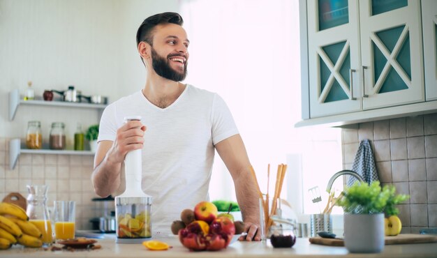 Beau jeune homme souriant sportif dans la cuisine prépare un smoothie