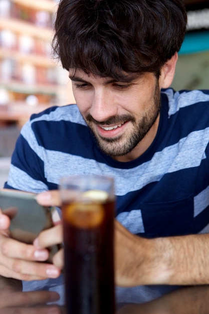 Beau jeune homme souriant avec téléphone portable au café en plein air