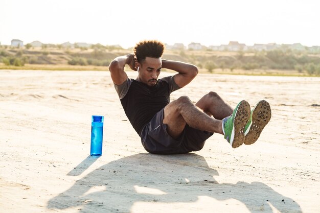 Beau jeune homme sportif fort, écouter de la musique avec des écouteurs à l'extérieur fait des exercices