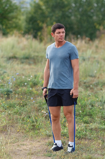 Beau jeune homme sportif musclé exerçant à l'extérieur en plein air avec un élastique. Fit, fitness, exercice, entraînement et concept de mode de vie sain.