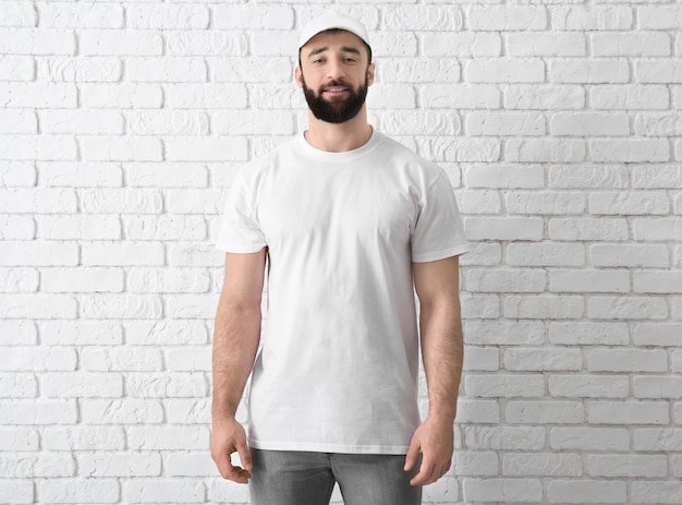 Beau jeune homme en t-shirt blanc élégant près du mur de briques Maquette pour le design