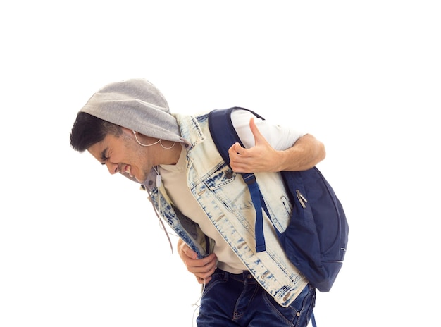 Beau jeune homme en T-shirt blanc et veste en jean avec sac à dos bleu à l'aide d'écouteurs et de danse