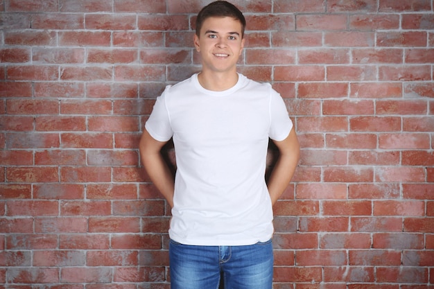 Photo beau jeune homme en t-shirt blanc vierge debout contre le mur de briques