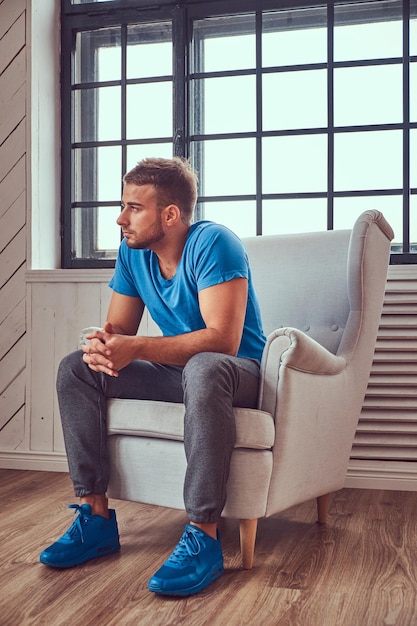 Un beau jeune homme en t-shirt bleu et baskets se détendant assis sur une chaise.