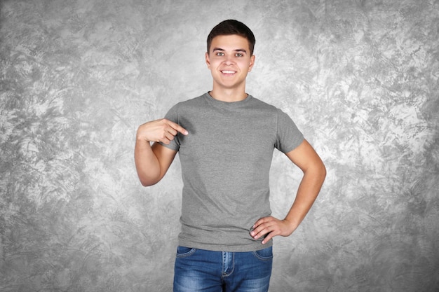 Beau jeune homme en t-shirt gris blanc debout contre un mur texturé