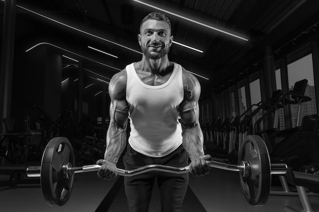 Beau jeune homme travaillant avec une barre dans la salle de gym. Pompage des biceps. Concept de remise en forme et de musculation.