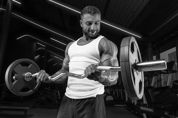 Beau jeune homme travaillant avec une barre dans la salle de gym. Pompage des biceps. Concept de remise en forme et de musculation.