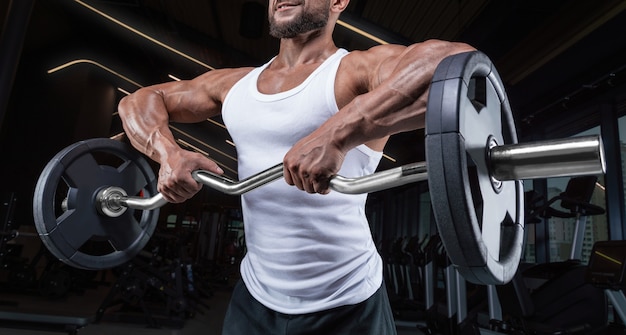 Beau jeune homme travaillant avec une barre dans la salle de gym. Pompage d'épaule. Barbell tire au menton. Concept de remise en forme et de musculation.