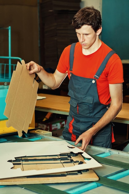 Beau jeune homme travaillant dans la fabrication avec des boîtes à l'usine pour la production d'emballages en carton