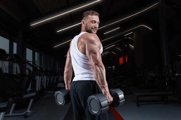 Beau jeune homme travaillant avec des haltères dans la salle de gym. Pompage d'épaule. Concept de remise en forme et de musculation.