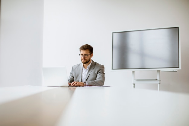 Beau jeune homme travaillant sur ordinateur portable dans un bureau lumineux avec grand écran derrière lui