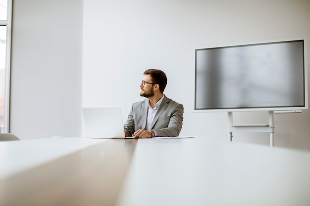 Beau jeune homme travaillant sur ordinateur portable dans un bureau lumineux avec grand écran derrière lui