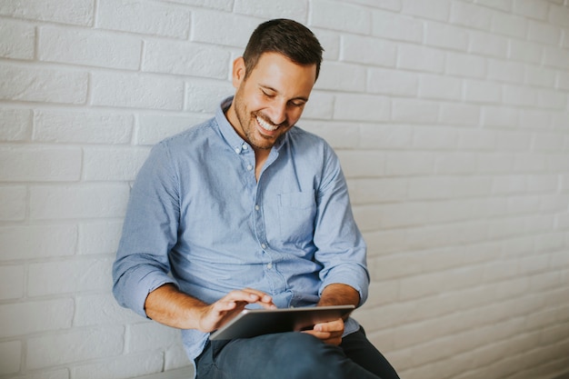 Beau jeune homme travaillant avec une tablette numérique dans la chambre