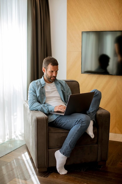 Beau jeune homme utilisant un ordinateur portable dans le salon