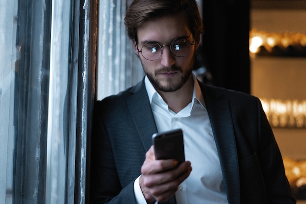 Beau jeune homme utilisant un téléphone intelligent pendant la nuit. Gros plan du visage d'un homme d'affaires heureux, messagerie sur téléphone portable la nuit au café.