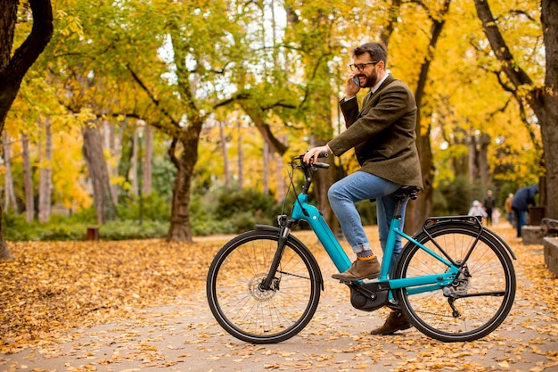 Beau jeune homme utilisant un téléphone portable sur un vélo électrique au parc d'automne