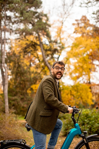 Beau jeune homme avec vélo électrique dans le parc en automne