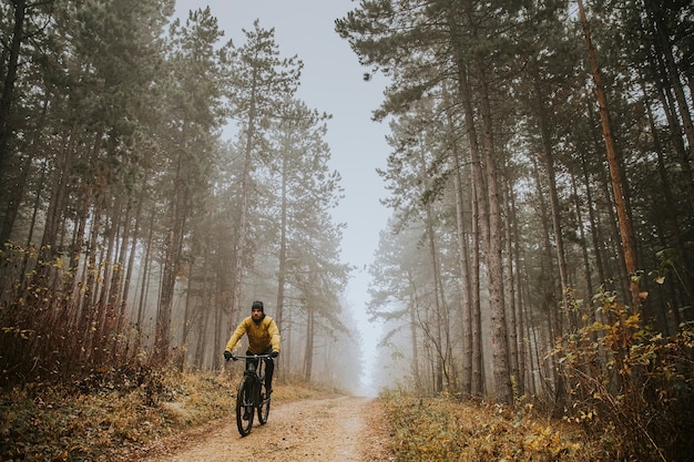 Beau jeune homme à vélo à travers la forêt d'automne