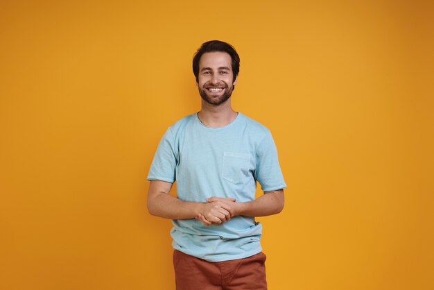 Beau jeune homme en vêtements décontractés regardant la caméra et souriant tout en se tenant contre un ba jaune...