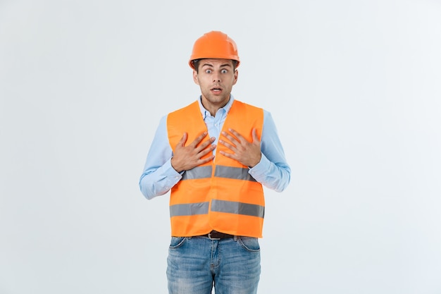 Beau Jeune Ingénieur Sur Fond Blanc Portant Un Casque De Sécurité Avec Un Visage Sérieux Et Une Main Choquée Par La Honte De L'erreur, L'expression De La Peur, Effrayée En Silence, Concept Secret