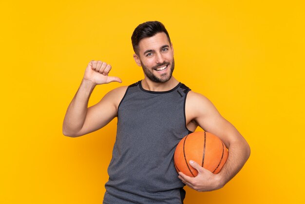 Beau jeune joueur de basket-ball sur un mur blanc isolé, fier et satisfait de lui-même