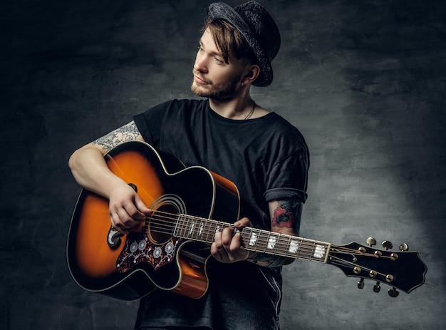 Beau jeune joueur de blues de guitare acoustique avec des tatouages sur les bras exécutant ses compétences musicales.