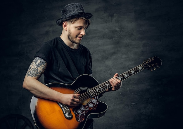 Beau jeune joueur de blues de guitare acoustique avec des tatouages sur les bras exécutant ses compétences musicales.