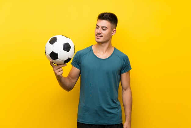 Beau jeune joueur de football homme sur mur jaune isolé avec expression heureuse