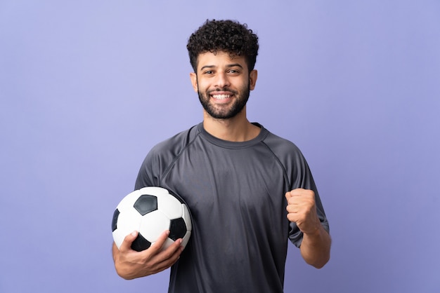 Beau jeune joueur de football marocain homme plus isolé sur mur violet célébrant une victoire en position de vainqueur