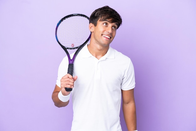 Beau jeune joueur de tennis homme isolé sur fond ocre pensant à une idée tout en levant les yeux