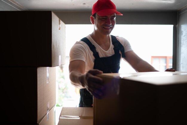 Beau jeune livreur à bonnet rouge et gants tenant une boîte dans le camion