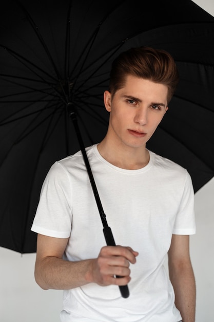 Beau jeune mannequin en t-shirt blanc avec parapluie noir en studio