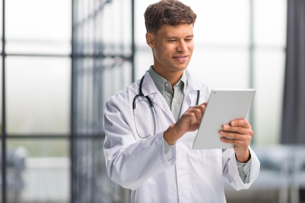 Beau jeune médecin sympathique dans le couloir de l'hôpital regardant la caméra en souriant