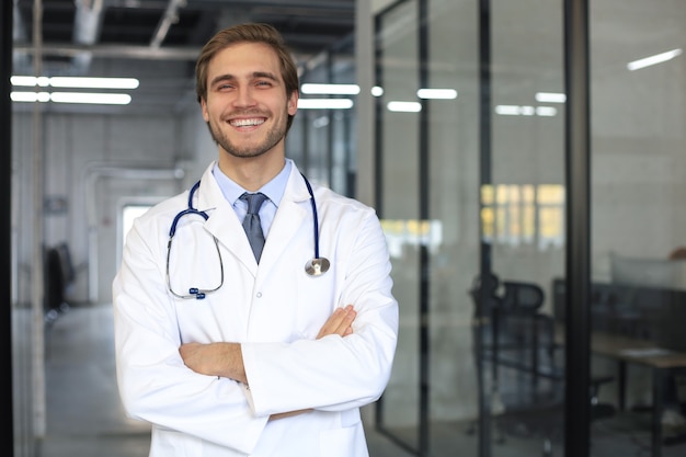 Beau jeune médecin sympathique dans le couloir de l'hôpital regardant la caméra, souriant.