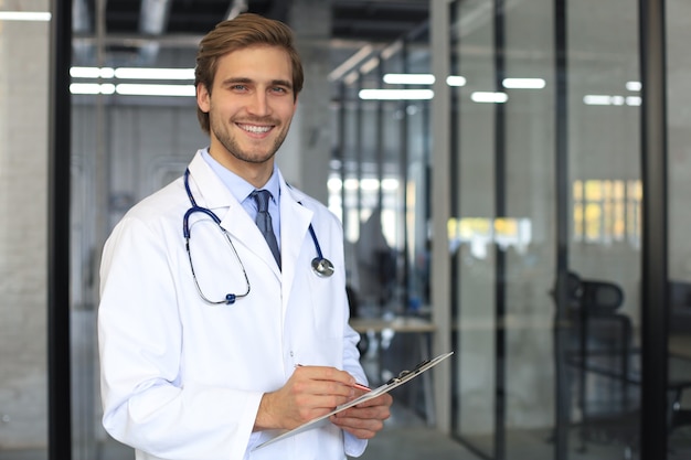 Beau jeune médecin sympathique dans le couloir de l'hôpital regardant la caméra, souriant.